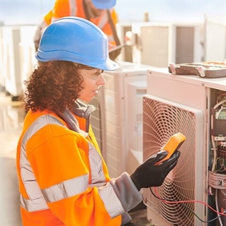 Woman with blue hardhat and orange vest working on HVAC unit using diagnostic materials